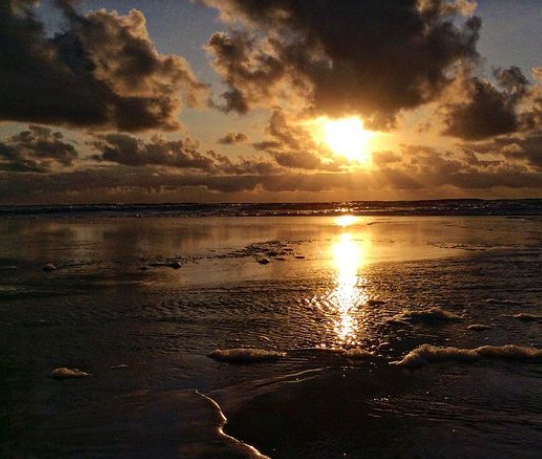 coucher de soleil au bord de l'eau. Le ciel comporte des nuages.