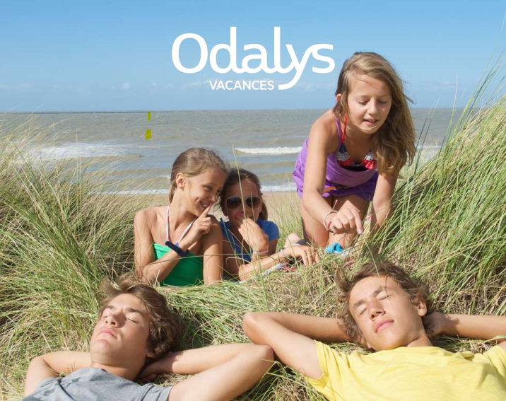 3 enfants et 2 adolescents allongés sur une dune devant la mer en arrière plan